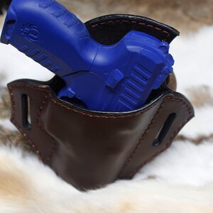 May include: A blue handgun in a brown leather holster. The holster has a belt loop and is designed to be worn on the hip.