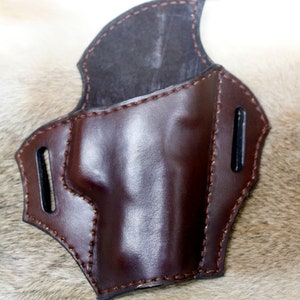 May include: A brown leather holster with stitching detail. The holster has two belt loops on the back.
