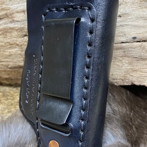 Peut inclure: Un &eacute;tui en cuir bleu fonc&eacute; avec une pince m&eacute;tallique et des coutures. L'&eacute;tui est con&ccedil;u pour un pistolet Ruger LCR. "Smith River Holsters" est imprim&eacute; sur le c&ocirc;t&eacute;.