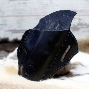 May include: A black leather holster with a stitched design and a flap. The holster is made of high-quality leather and has a smooth finish.