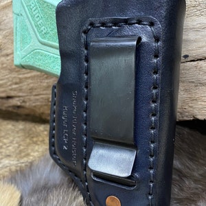 Peut inclure: Un &eacute;tui en cuir noir avec un clip pour un pistolet Ruger LCP 2. L'&eacute;tui est cousu avec du fil blanc et porte une &eacute;tiquette Snake River Holsters.