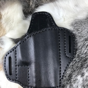 May include: Black leather holster with stitching detail. The holster has two cutouts on the side.