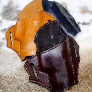 May include: Three leather holsters in different colors: brown, tan, and black. The holsters are made of high-quality leather and have a stitched design.