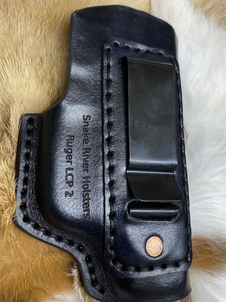 Peut inclure: &Eacute;tui en cuir noir avec un clip en m&eacute;tal et le texte "Snake River Holsters Ruger LCP 2" grav&eacute; sur le c&ocirc;t&eacute;.