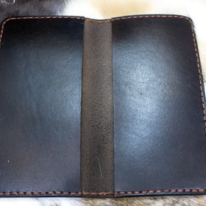 May include: A black leather notebook with a brown stitching detail. The notebook is closed and lying flat on a white surface.