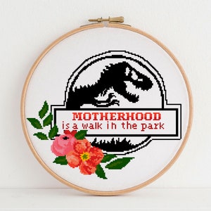 May include: A white embroidery hoop with a black and white illustration of a dinosaur with the text "MOTHERHOOD is a walk in the park". The hoop is decorated with pink and red flowers.