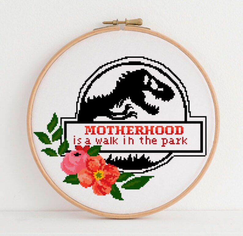 May include: A white embroidery hoop with a black and white illustration of a dinosaur with the text "MOTHERHOOD is a walk in the park". The hoop is decorated with pink and red flowers.