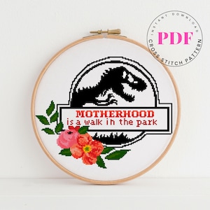 May include: Cross stitch pattern featuring a black dinosaur silhouette with the text "Motherhood is a walk in the park" in red and white. The pattern is surrounded by green leaves and pink and red flowers.
