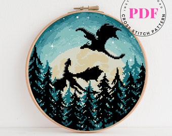 May include: Cross stitch pattern featuring a silhouette of a dragon flying over a forest with a full moon in the background. The pattern is in a wooden embroidery hoop.