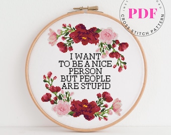 May include: A cross-stitch pattern in a wooden hoop with the text "I WANT TO BE A NICE PERSON BUT PEOPLE ARE STUPID." The design includes a floral wreath in shades of red and pink. A PDF download is indicated.