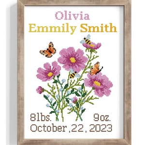 May include: Cross-stitch artwork in a wooden frame featuring the name "Olivia Emmily Smith" in yellow and pink. The design includes pink flowers, butterflies, and bees. The text below reads "8lbs. 9oz. October 22, 2023".