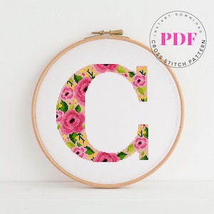Op de afbeelding: Een kruissteekpatroon van de letter "C" in een houten borduurring. De letter is gevuld met roze rozen en groene bladeren. De woorden "INSTANT DOWNLOAD PDF CROSS STITCH PATTERN" staan in een cirkel.