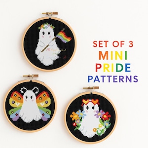 May include: Set of three mini Pride cross-stitch patterns. Each pattern features a white ghost with a different design: a rainbow flag, butterfly wings, and a floral wreath. The patterns are displayed in wooden embroidery hoops.