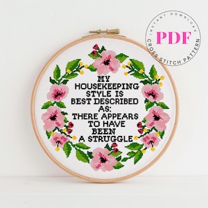 May include: A cross-stitch embroidery hoop with the text "MY HOUSEKEEPING STYLE IS BEST DESCRIBED AS: THERE APPEARS TO HAVE BEEN A STRUGGLE." The design features pink flowers and green leaves. A PDF download is indicated.