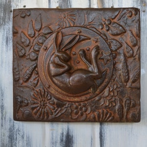 May include: A brown metal wall plaque with a raised design of a rabbit sleeping on a crescent moon surrounded by flowers and leaves.
