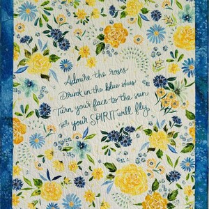 May include: A floral quilt with a white background, featuring yellow and blue flowers and green leaves. The quilt has a blue border and includes the text "Admire the roses, Drink in the blue skies, Turn your face to the sun and your SPIRIT will fly."