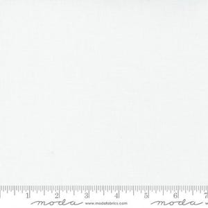 May include: A close-up of a white fabric with a subtle woven texture. The fabric is plain and evenly lit, with a ruler along the bottom edge. The fabric is likely used for quilting or sewing projects.