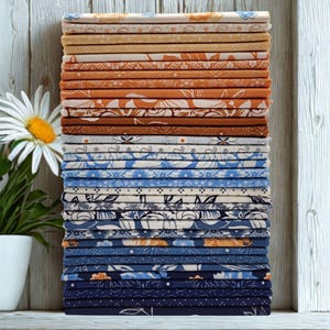 May include: A tall stack of folded fabric squares featuring a variety of patterns including floral, geometric, and dotted designs in a color palette ranging from light cream and warm orange to shades of blue and deep navy, arranged in a vertical column.