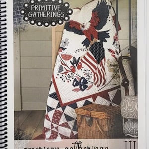 Peut inclure: Un livre à spirales intitulé "Primitive Gatherings" présentant une courtepointe avec un drapeau américain et un motif d'aigle. La courtepointe est blanche avec des accents rouges, blancs et bleus. Un panier en osier est au premier plan. Le texte "american gatherings III" est en bas.