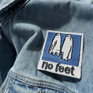 May include: A blue denim jacket with a white embroidered patch that says "no feet" and features two white ghosts.