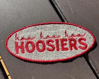 May include: A white oval embroidered patch with red stitching. The patch says "Hoosiers" in red lettering.
