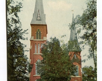 May include: Vintage postcard featuring Saint Patrick's Church in Lewiston, Maine. The church is constructed of red brick with two tall spires topped with crosses. Lush green trees frame the church, and the sky is a pale blue.