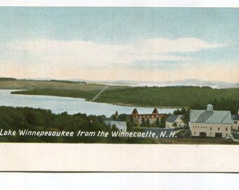 May include: A vintage postcard featuring a landscape view of Lake Winnipesaukee from the Winnecoette, N.H. The scene displays a large body of water, dense green forests, and several buildings including a large white structure with a cupola.