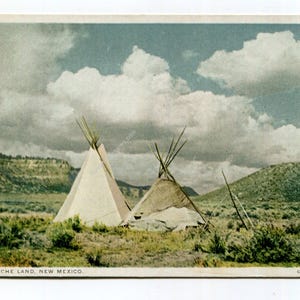 May include: Vintage postcard featuring two teepees in a grassy field under a cloudy sky. The landscape includes rolling hills and sparse vegetation. The text at the bottom reads "In Apache Land, New Mexico."