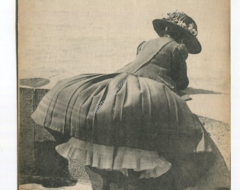 May include: A vintage sepia-toned postcard featuring a person in a dark, wide-brimmed hat with floral details, wearing a long, full-skirted dress with a ruffled petticoat underneath. The text reads LE TREPORT, Au bout de la Jetée, Un coup de vent.