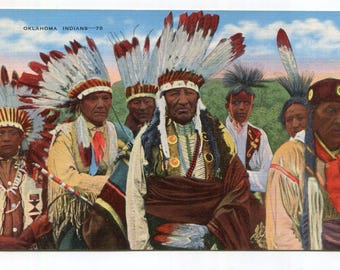 May include: A vintage postcard titled OKLAHOMA INDIANS-78 featuring a group of Indigenous people wearing traditional feathered headdresses, beaded necklaces, and fringed garments against a landscape background with a blue sky.