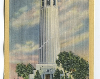May include: A vintage postcard featuring the Coit Memorial on Telegraph Hill in San Francisco, California. The tall, white, fluted concrete tower stands against a cloudy sky, surrounded by green trees, red flowers, and two vintage cars.