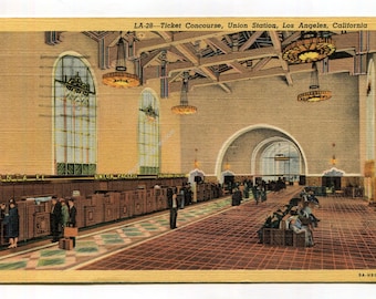 May include: A vintage postcard showing the Ticket Concourse at Union Station in Los Angeles, California. The interior features high ceilings with exposed wooden beams, large arched windows, hanging chandeliers, and a long wooden ticket counter.