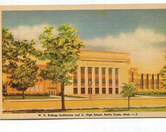 May include: A vintage postcard illustration of the W. K. Kellogg Auditorium and Jr. High School in Battle Creek, Michigan. The building features a tan facade with tall columns, surrounded by green trees and a clear blue sky.