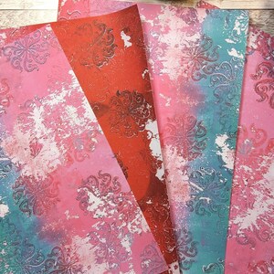 May include: Four sheets of decorative paper with a distressed, vintage look. The paper features a damask pattern in shades of pink, blue, and white.