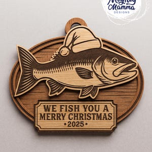 May include: Wooden Christmas ornament featuring a fish wearing a Santa hat. The ornament has a dark brown fish design on a lighter wood background. Text on the ornament reads "WE FISH YOU A MERRY CHRISTMAS &bull;2025."