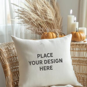 May include: A white cushion with the text "PLACE YOUR DESIGN HERE" on a wicker chair. The cushion is surrounded by dried pampas grass, candles, and pumpkins. The text "WORKS GREAT WITH CANVA & PHOTOSHOP" is at the bottom of the image.