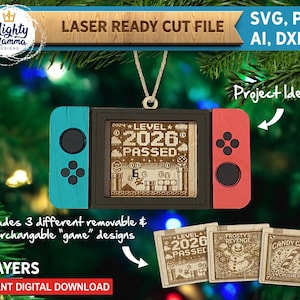 Könnte beinhalten: Ein lasergeschnittenes Holzornament in Form einer tragbaren Spielkonsole mit blauem linken Controller, rotem rechten Controller und schwarzem Mittelbildschirm. Der Bildschirm zeigt den Text Level 2026 Passed. Enthält drei austauschbare Spieleinsätze.