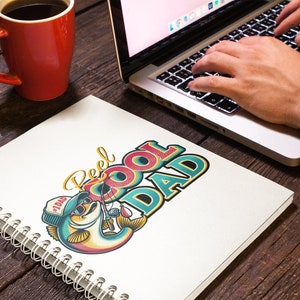 Peut inclure: Un carnet &agrave; spirales blanc avec une illustration color&eacute;e d'un poisson tenant une canne &agrave; p&ecirc;che. Le texte "Reel Cool Dad" est &eacute;crit en lettres color&eacute;es au-dessus du poisson. Le poisson porte un chapeau qui dit "#1 Dad".