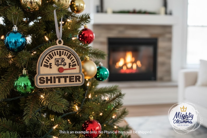 May include: A wooden Christmas ornament shaped like a gauge with a camper icon and the word "SHITTER". The ornament is hanging on a Christmas tree with colorful ornaments and lights. The background shows a fireplace.