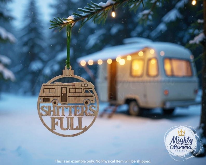May include: A wooden Christmas ornament with a camper design and the words "SHITTERS FULL". The ornament is hanging from a green ribbon against a snowy winter backdrop. A vintage camper is in the background.