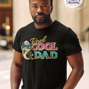 Peut inclure: Un t-shirt noir avec un motif graphique d'un poisson de dessin anim&eacute; portant des lunettes de soleil et tenant une canne &agrave; p&ecirc;che. Le texte "Reel Cool Dad" est &eacute;crit dans une police r&eacute;tro color&eacute;e.