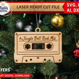 May include: A wooden cassette tape Christmas tree ornament with the text "A Jingle Bell Rock Mix". The ornament hangs on a Christmas tree decorated with red and gold baubles. The text "LASER READY CUT FILE" is at the top.