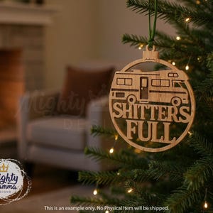 May include: A wooden Christmas ornament with a laser-cut design of a recreational vehicle and the phrase "SHITTER'S FULL". The ornament is hanging from a green ribbon on a Christmas tree.