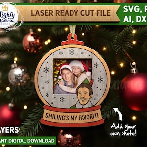 Op de afbeelding: Houten kerstornament met een fotolijst, sneeuwvlokken en de zin "Smiling's My Favorite". Het ornament is ontworpen om een foto te bevatten en heeft een stripfiguur. Het ontwerp is een laserklare snijbestand.