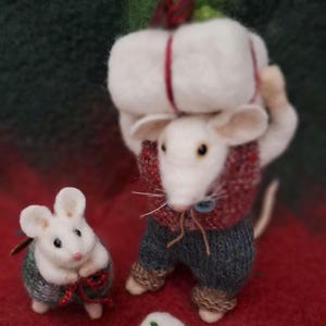 May include: A felted mouse figurine carrying a large white package with red string and green accents. Another mouse figurine sits nearby, and a small gift is on the red surface. The mouse wears a red sweater and blue pants.