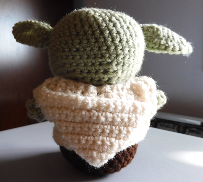 May include: A crocheted green and brown plush toy with large ears. The toy is wearing a white crocheted robe.