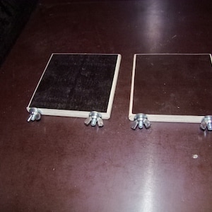 May include: Two square wooden blocks with black paint, each with two silver screws on the bottom.