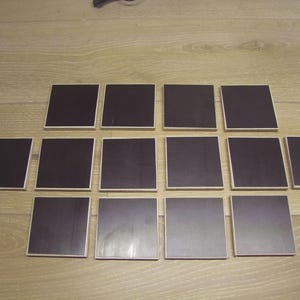 Op de afbeelding: Een set van 12 zwarte vierkante onderzetters met een houten frame.