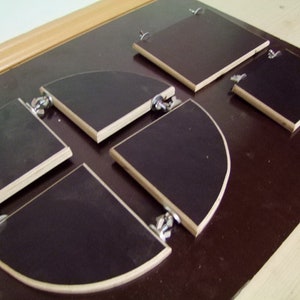 May include: Five wooden circular and square shaped pieces with metal hinges. The pieces are attached to a dark brown surface.