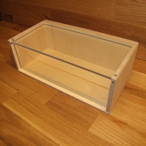 Könnte beinhalten: Eine Holzkiste mit einem durchsichtigen Glasdeckel. Die Kiste ist aus hellem Holz und hat ein schlichtes Design.